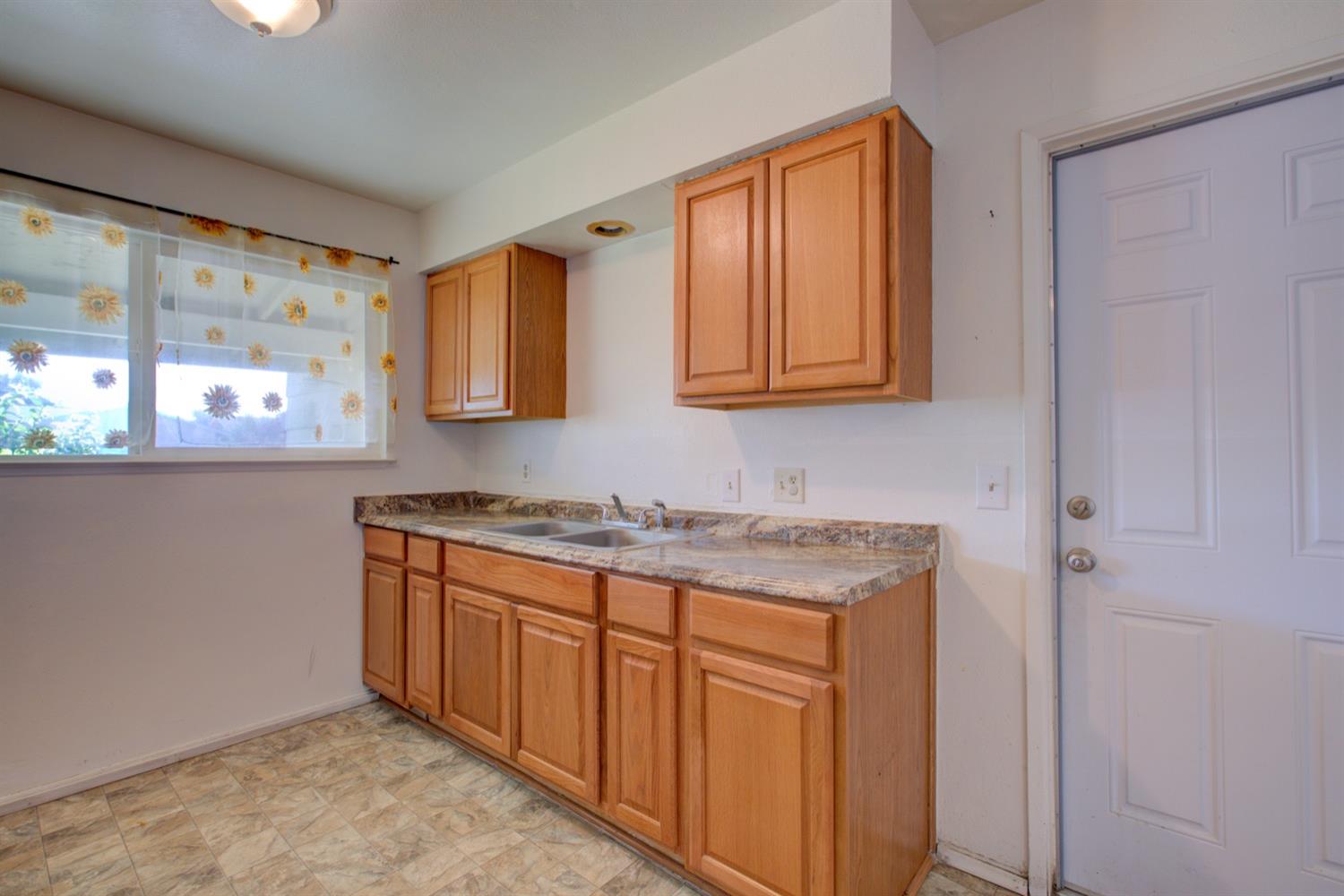 Kitchen with honey-colored cabinets, a double-basin sink, and sunflower curtains over the window.