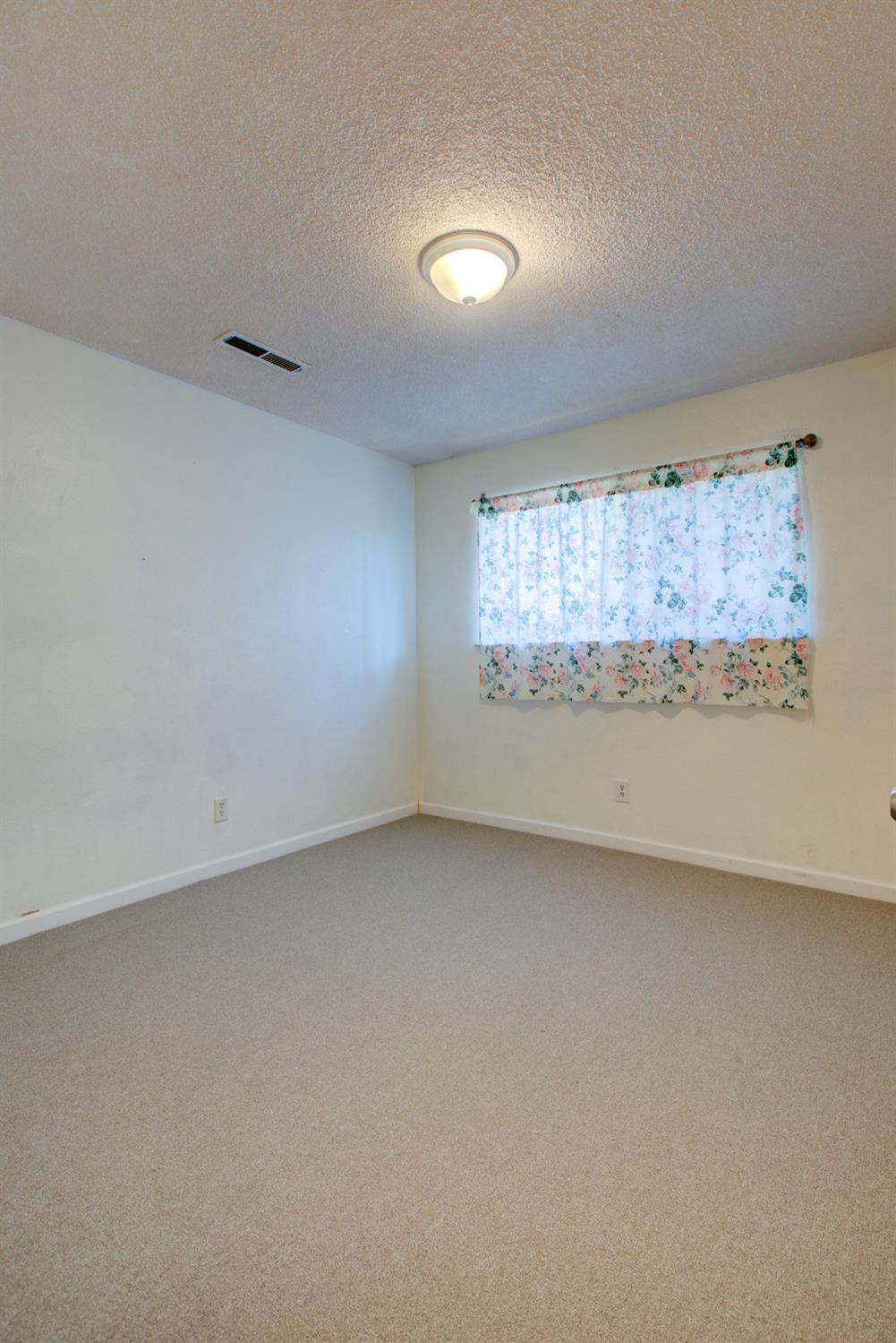 Empty bedroom with beige carpet and a floral-curtained window.