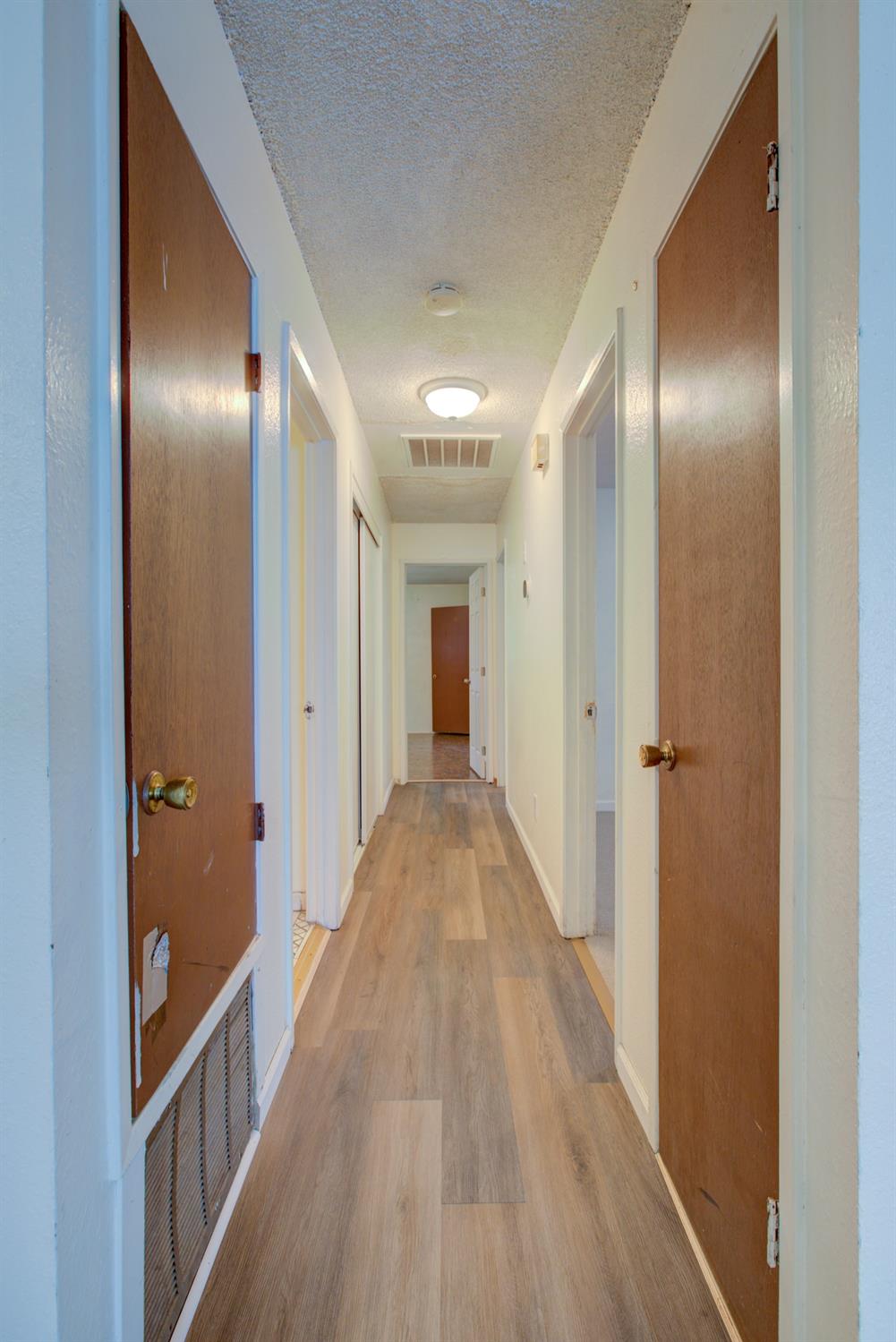 Long hallway with wood-look flooring, several wooden doors, and ceiling lights.