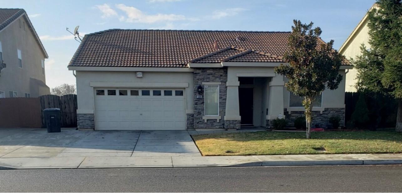Single-story home with a tiled roof, stone accents, two-car garage, and front lawn.