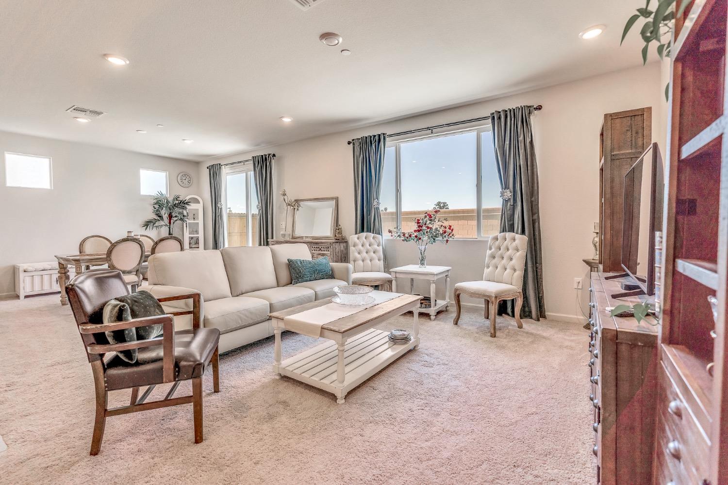 Staged living room with a cream sofa, wood coffee table, and large curtained windows.