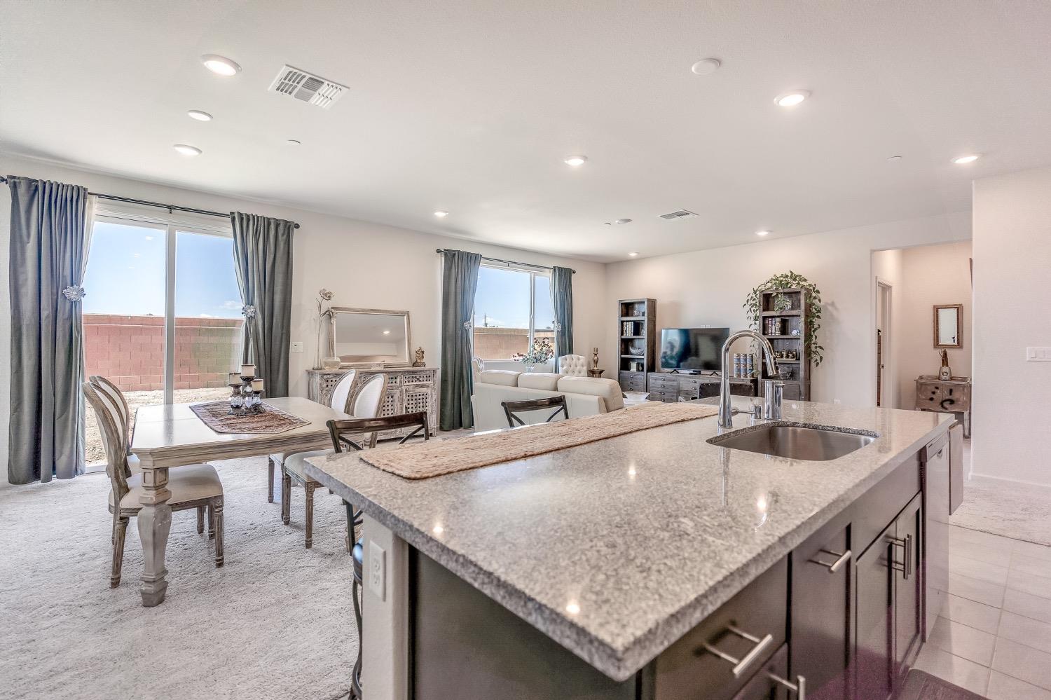 Open-plan kitchen with a large granite island, dining table, and furnished living room.