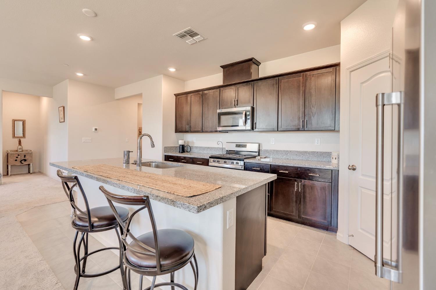 Kitchen with dark wood cabinets, granite breakfast bar, stainless steel appliances, and two stools.