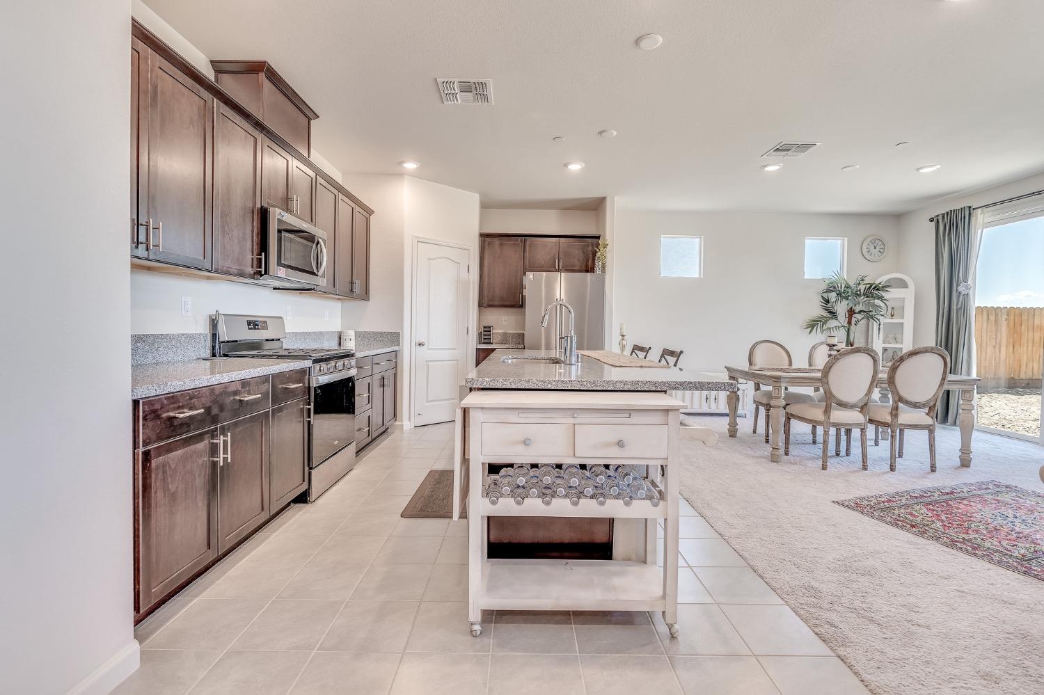 Open-plan kitchen with dark wood cabinets, granite island, and dining area beside sliding glass doors.
