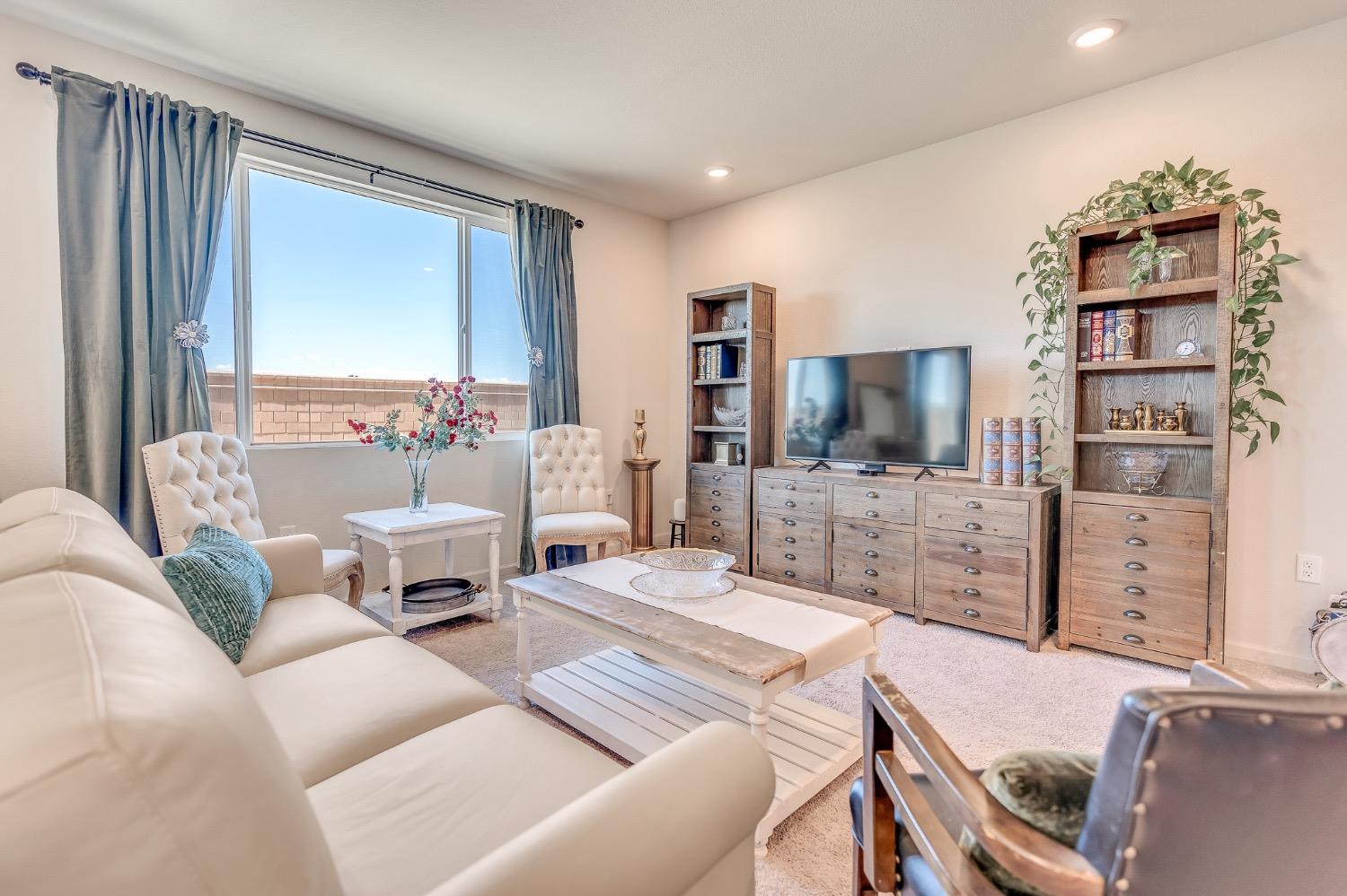 Living room with a white sectional, television, wood cabinets, and a large curtained window.