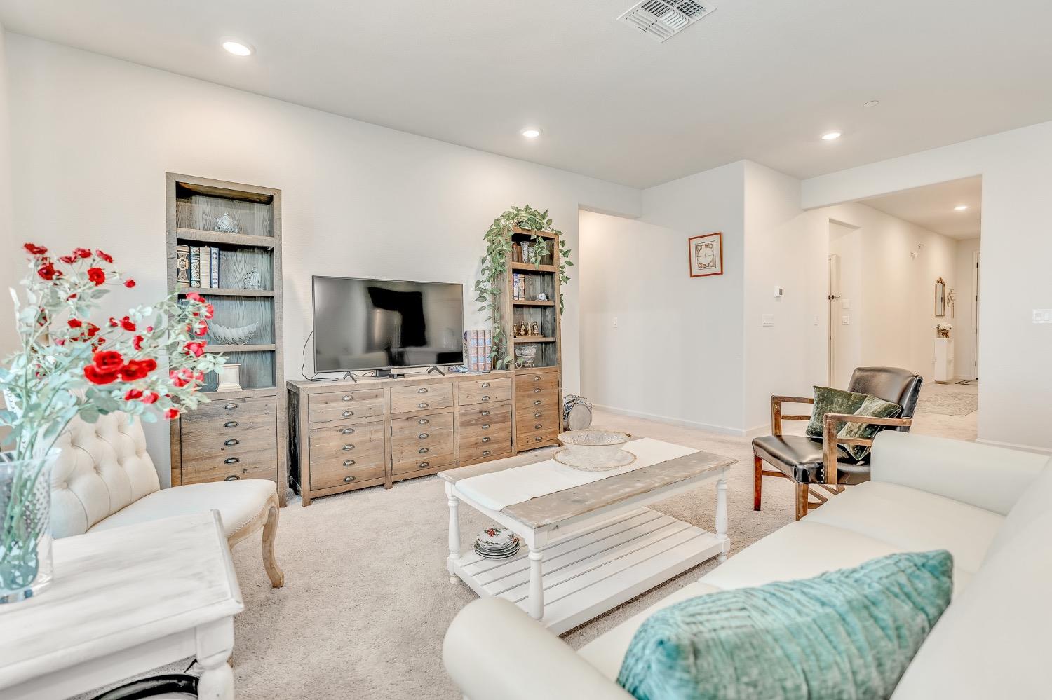 Furnished living room with white sofas, wooden bookcases, and a television.