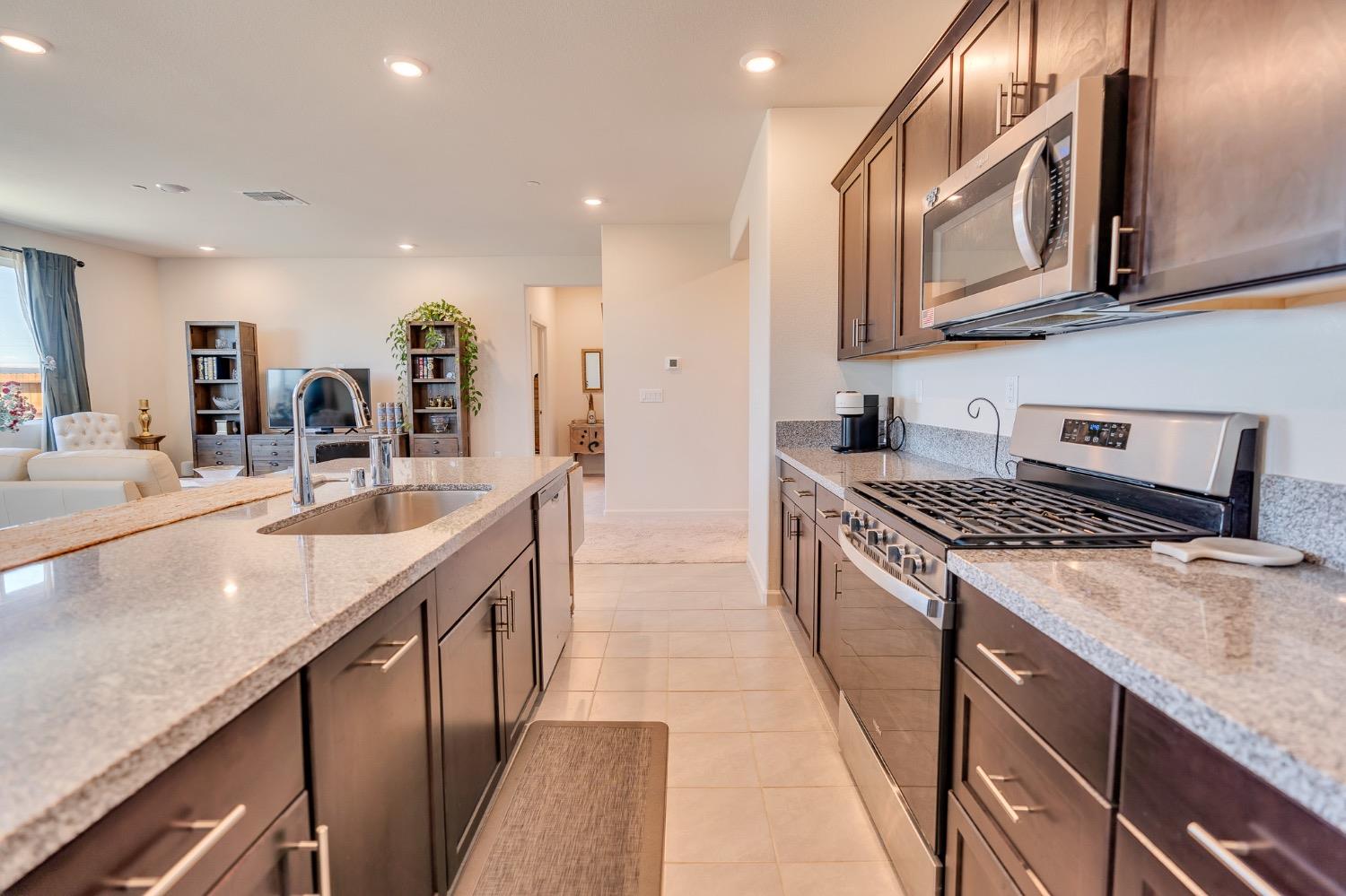 Kitchen with dark wood cabinets, granite island and counters, and stainless steel appliances opening to the living area.