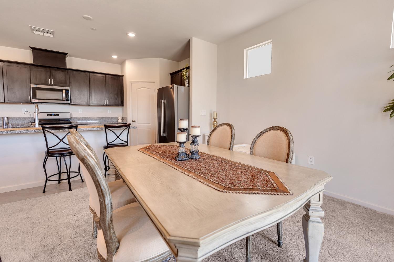 Dining area with a large wood table beside an open kitchen with dark cabinets.