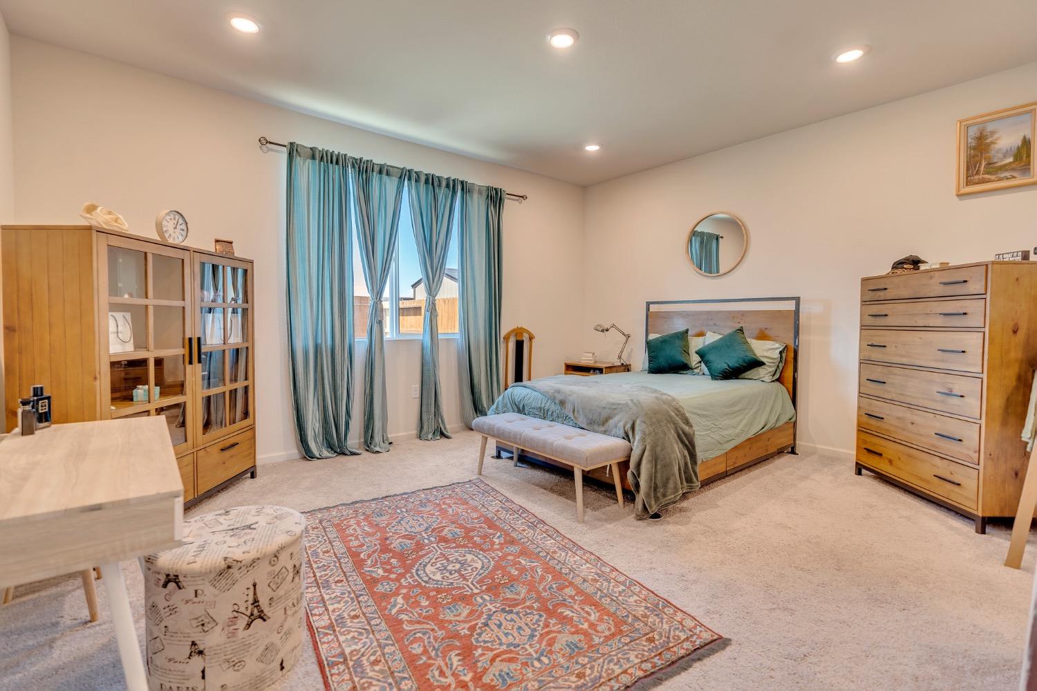 Bedroom with a wood bed, teal curtains and pillows, matching dressers, and a patterned rug.