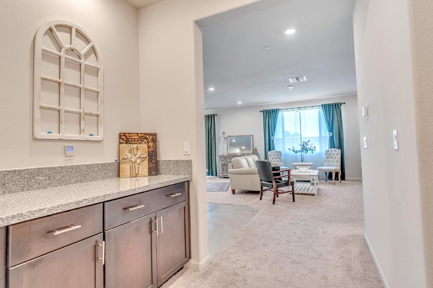 Hallway with dark cabinets and granite counter opening into a furnished living room with teal curtains.