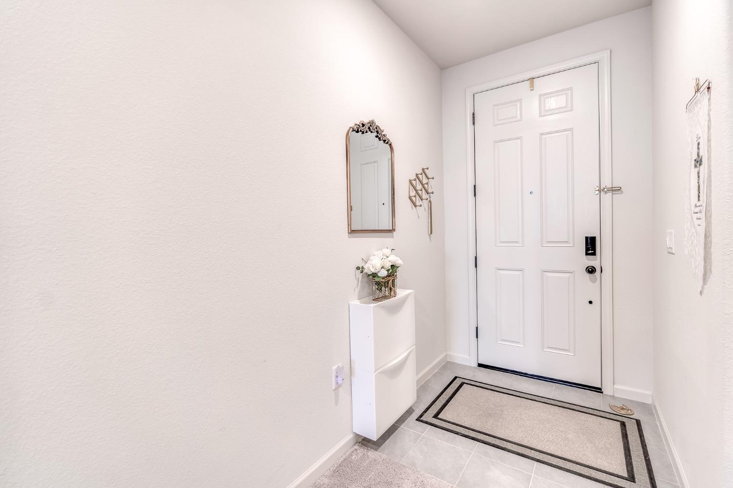 Entry foyer with a white paneled front door, gray tile floor, decorative mirror, and flower-topped console.