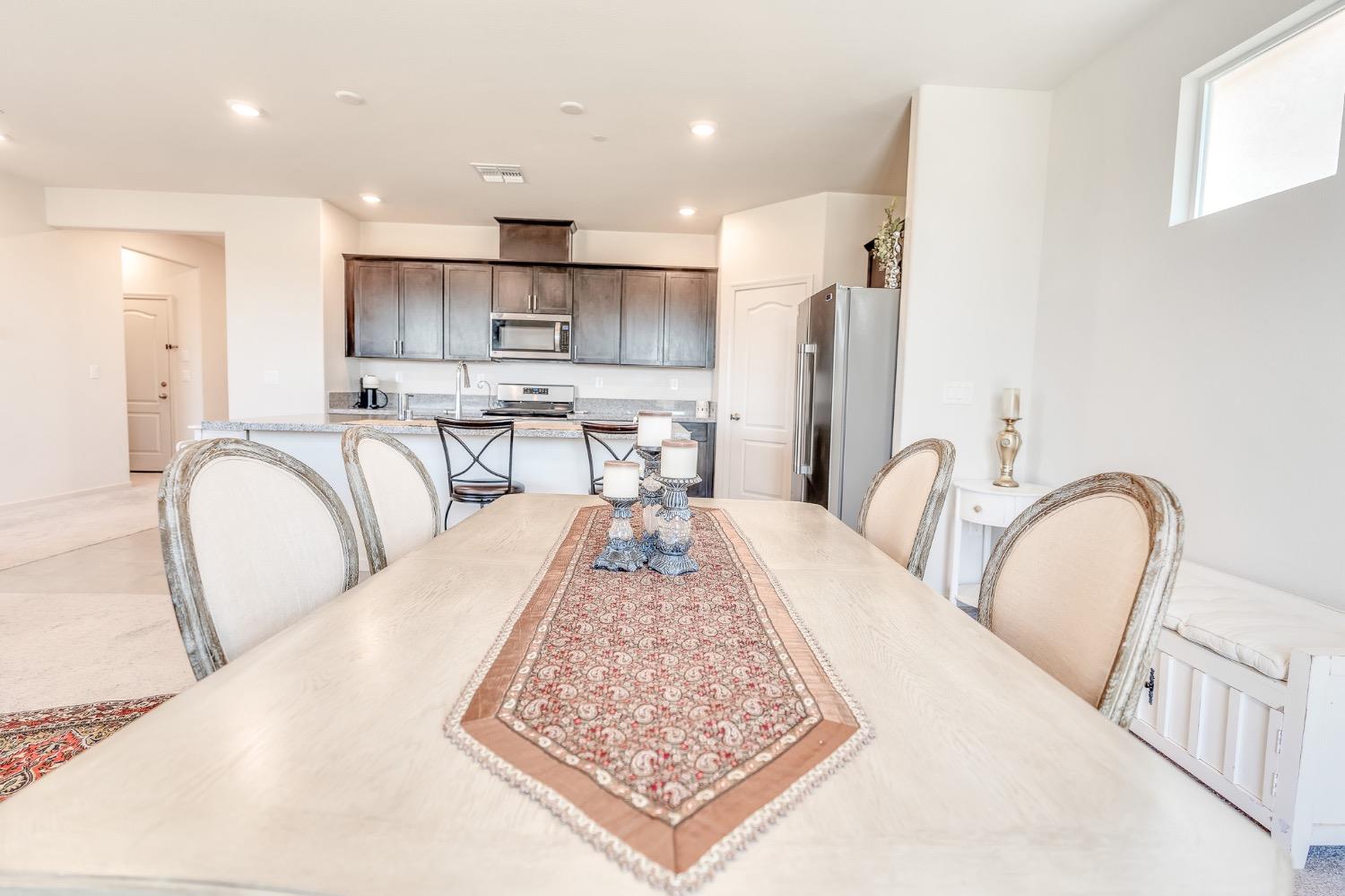 Dining table and chairs beside a bright open kitchen with dark cabinets.