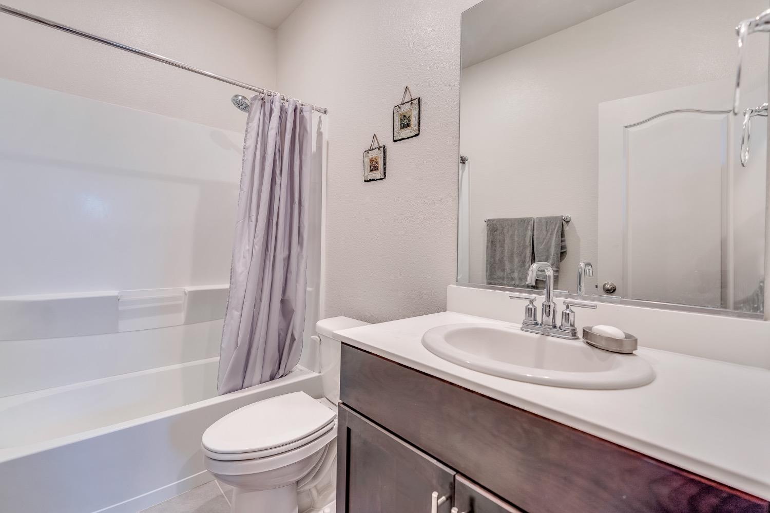 Bathroom with a white tub and shower, toilet, and dark wood vanity with an oval sink.
