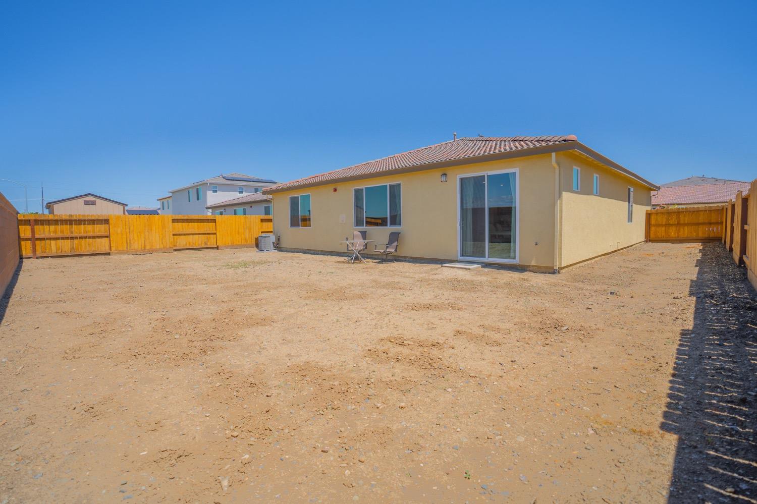 Single-story home viewed from its fenced dirt backyard, with a tiled roof and sliding glass doors.