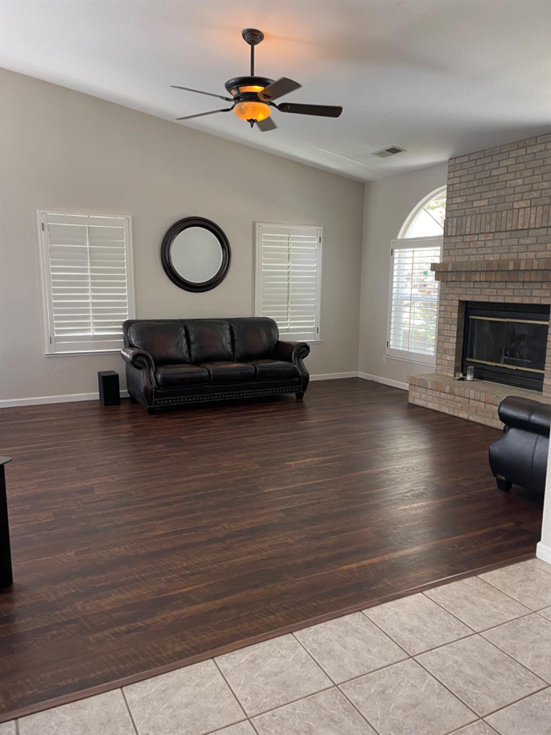 Living room with dark wood floors, a black leather sofa, and a brick fireplace.