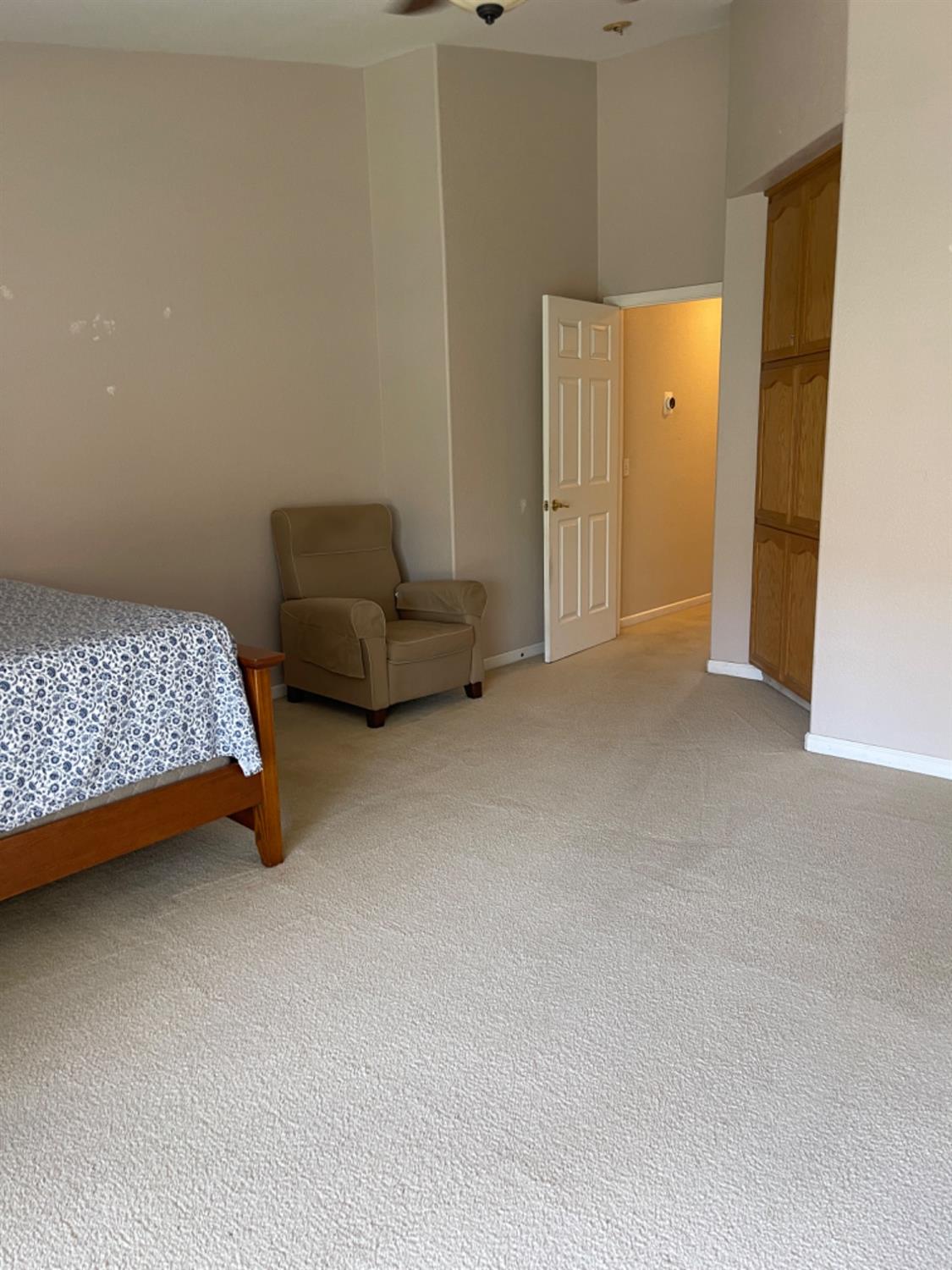 Bedroom with light carpet, a patterned bed, tan armchair, and built-in wooden cabinets.