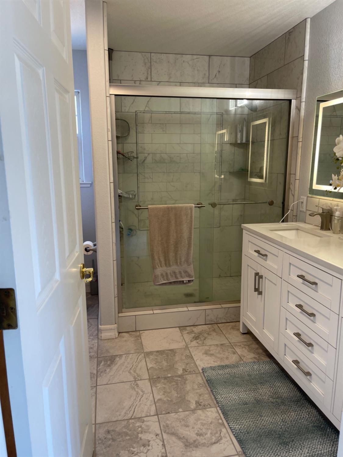 Bathroom with a glass-enclosed tiled shower and white double vanity.