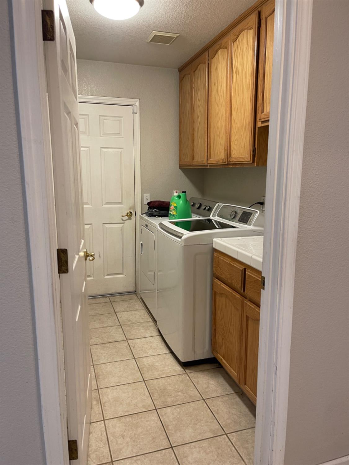 Laundry room with washer and dryer beneath wood cabinets and a tiled floor.