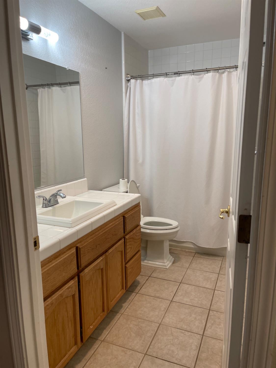 Bathroom with a wood vanity and large mirror beside a toilet and curtained tub.