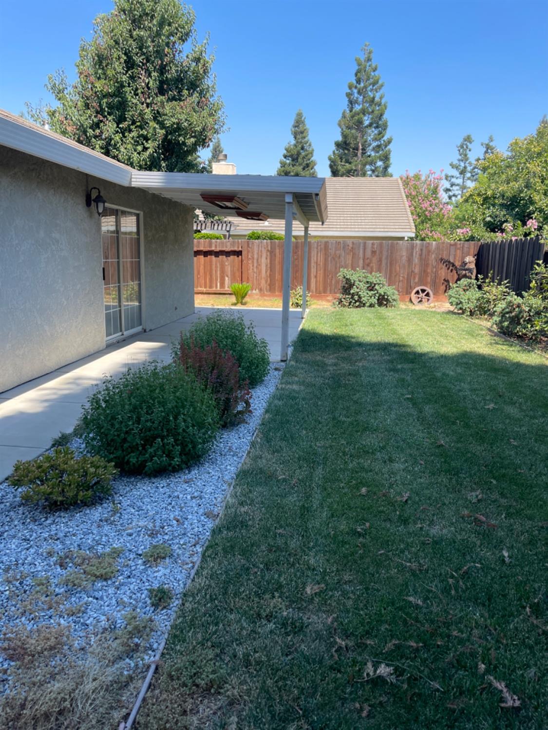 Backyard with a covered patio, green lawn, gravel-edged garden beds, and a wooden fence.