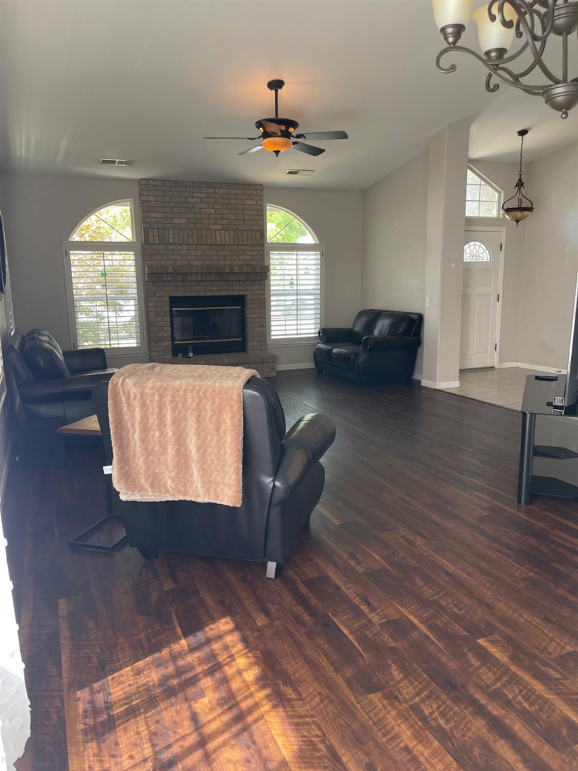 Living room with a brick fireplace, arched shuttered windows, leather seating, and dark hardwood floors.
