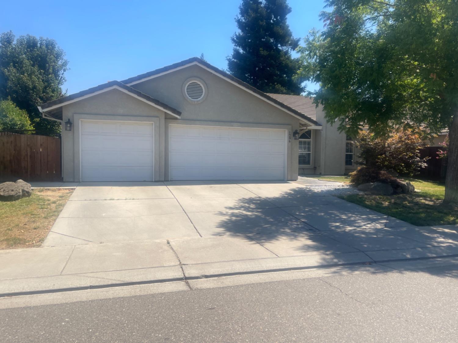 Gray stucco home with a two-car garage, wide driveway, and mature trees.