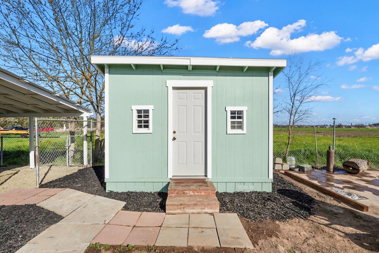 Mint-green backyard shed with white trim, a centered door, and paver steps.