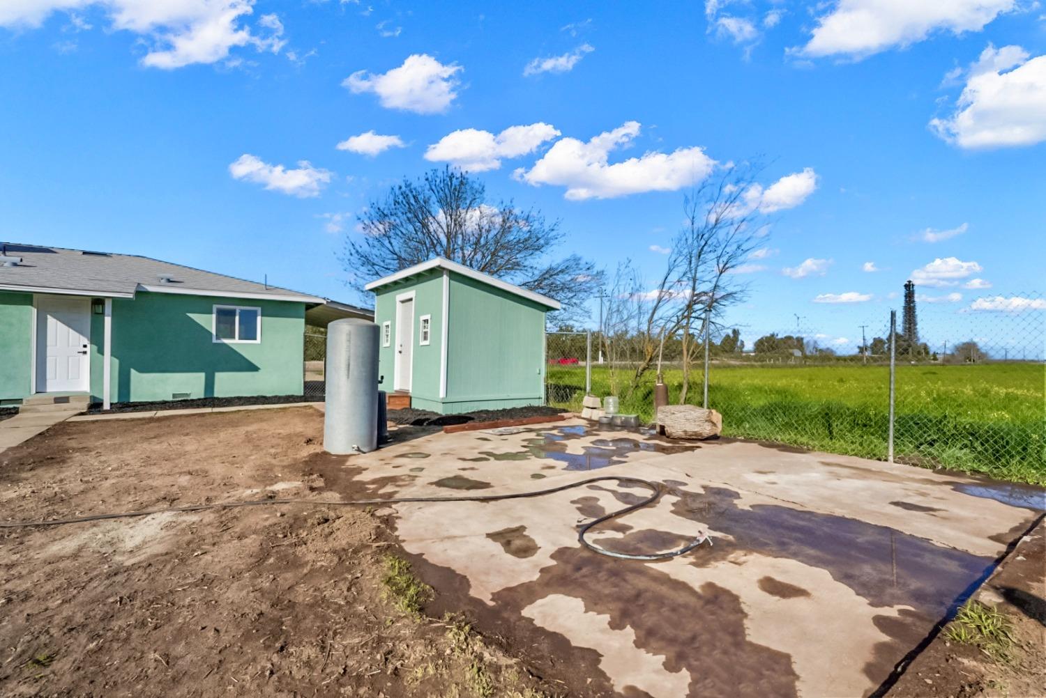 Green house and detached outbuilding beside a concrete pad and fenced grassy field.