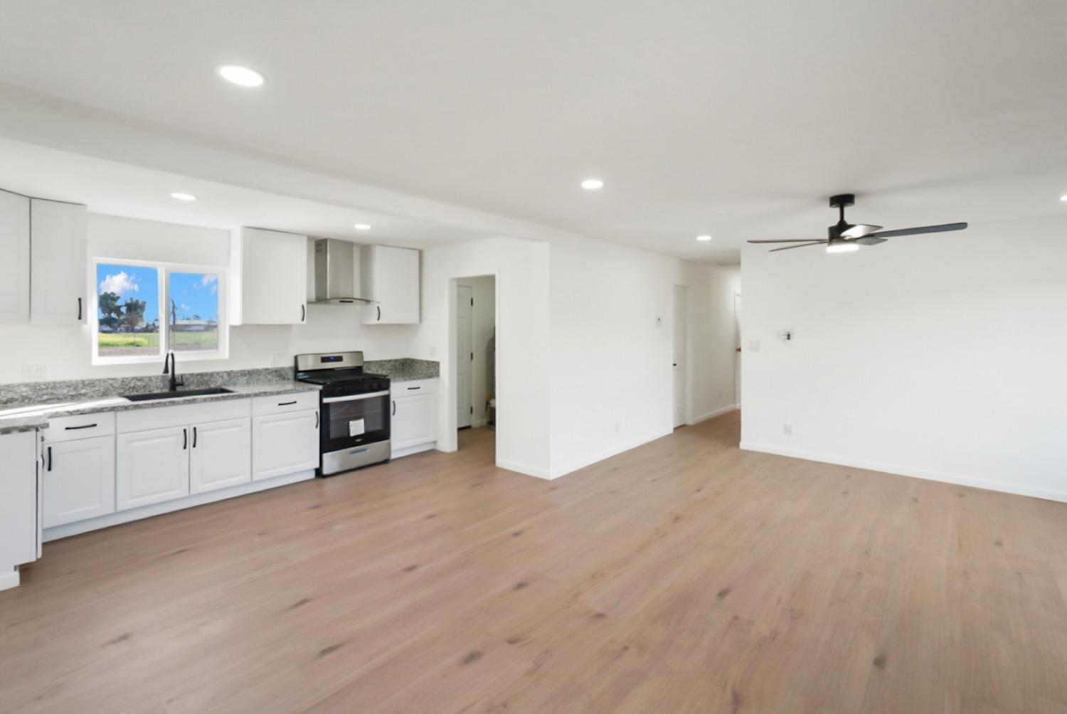 Unfurnished kitchen and living area with white cabinets, granite counters, and light wood floors.