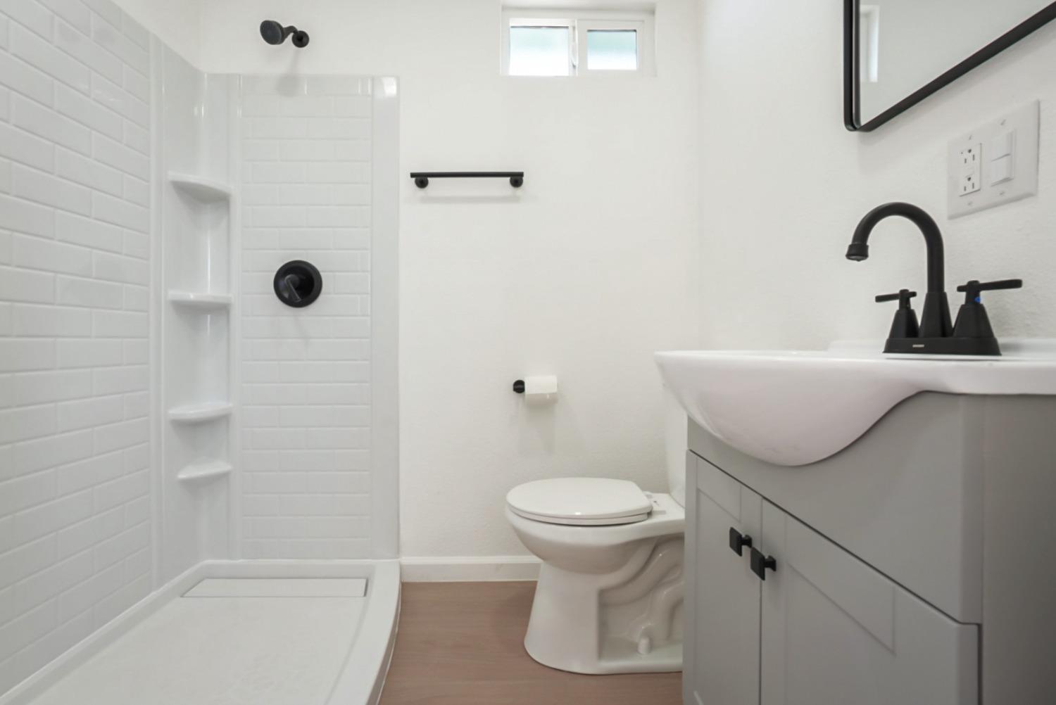 Bathroom with a subway-tile shower, built-in shelves, and gray vanity with black fixtures.