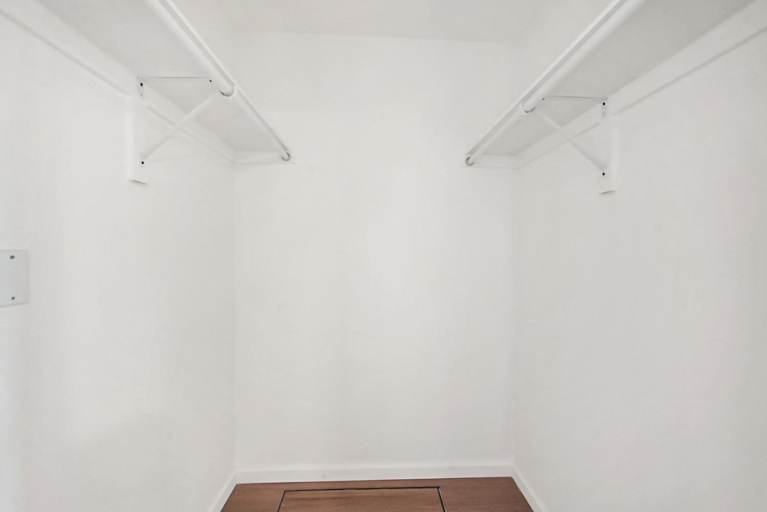Empty white closet with wire shelves on both sides and brown wood flooring.