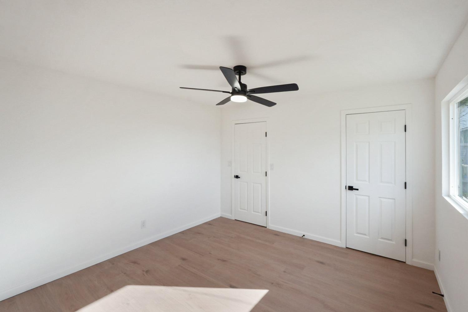 Empty bedroom with light wood-look flooring, a black ceiling fan, and two white doors.