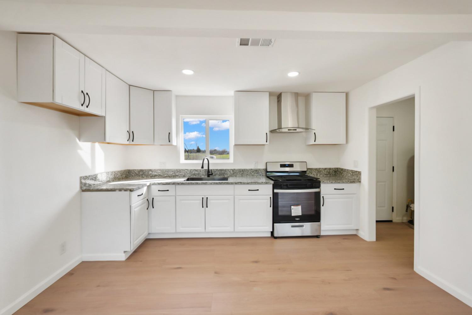 Kitchen with white cabinets, granite counters, a black-and-stainless range, and light wood floors.