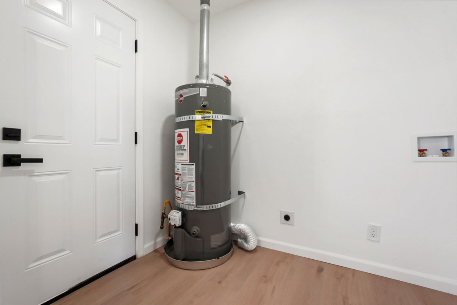 Tank water heater in a utility area beside a paneled door and wall plumbing connections.