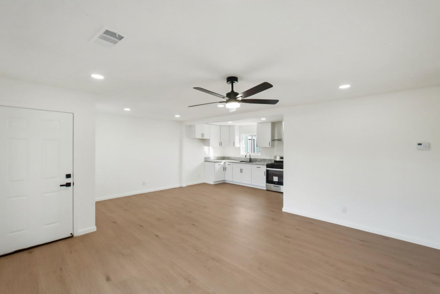 Open living area with light wood floors and a white kitchen with gray countertops.