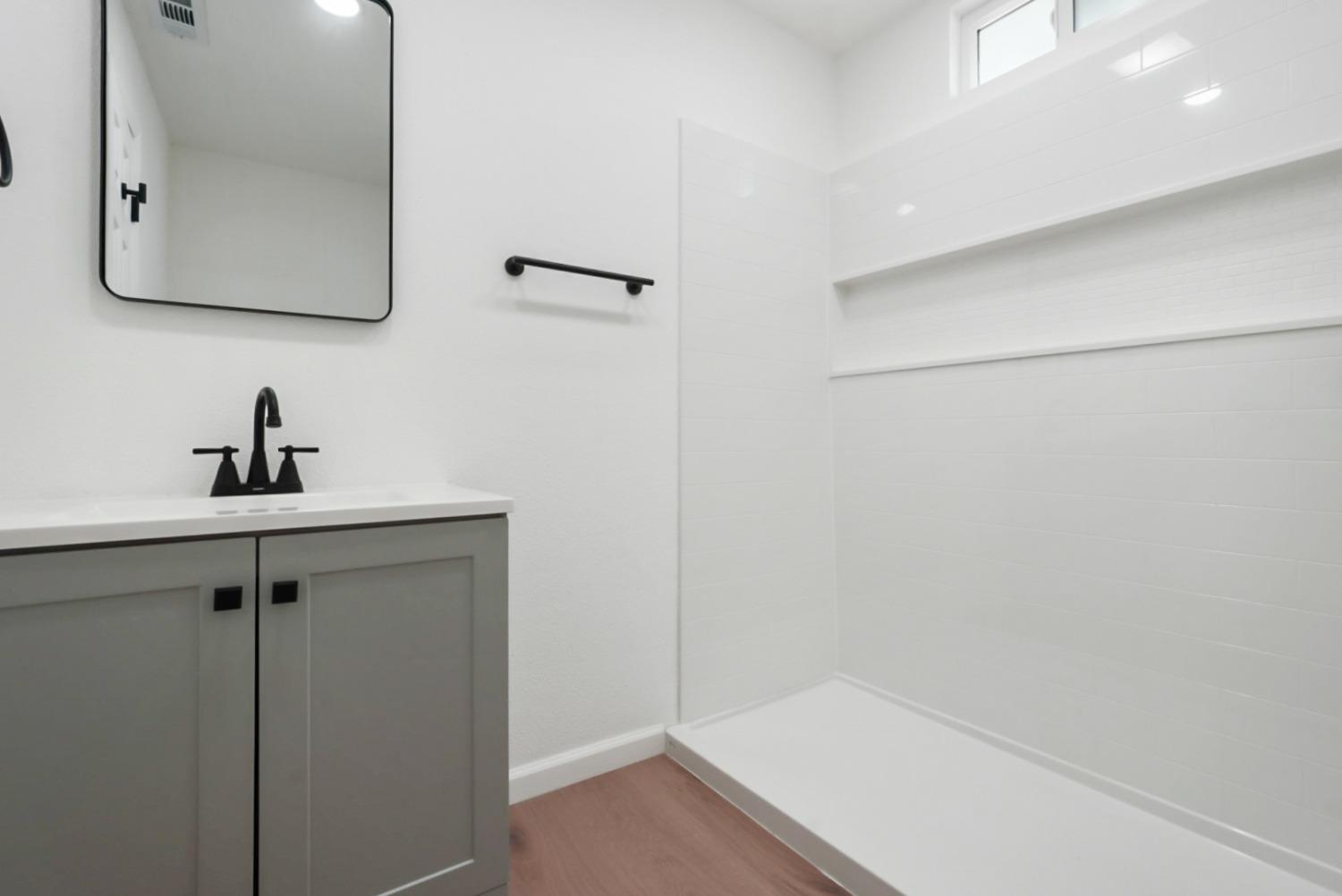 Bathroom with a white tiled walk-in shower and gray vanity with black fixtures.