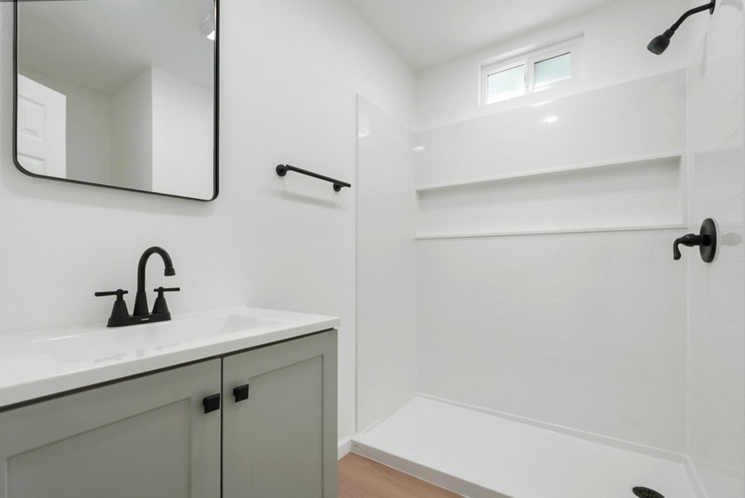 Modern bathroom with a gray vanity, black fixtures, and white tiled shower with a built-in niche.