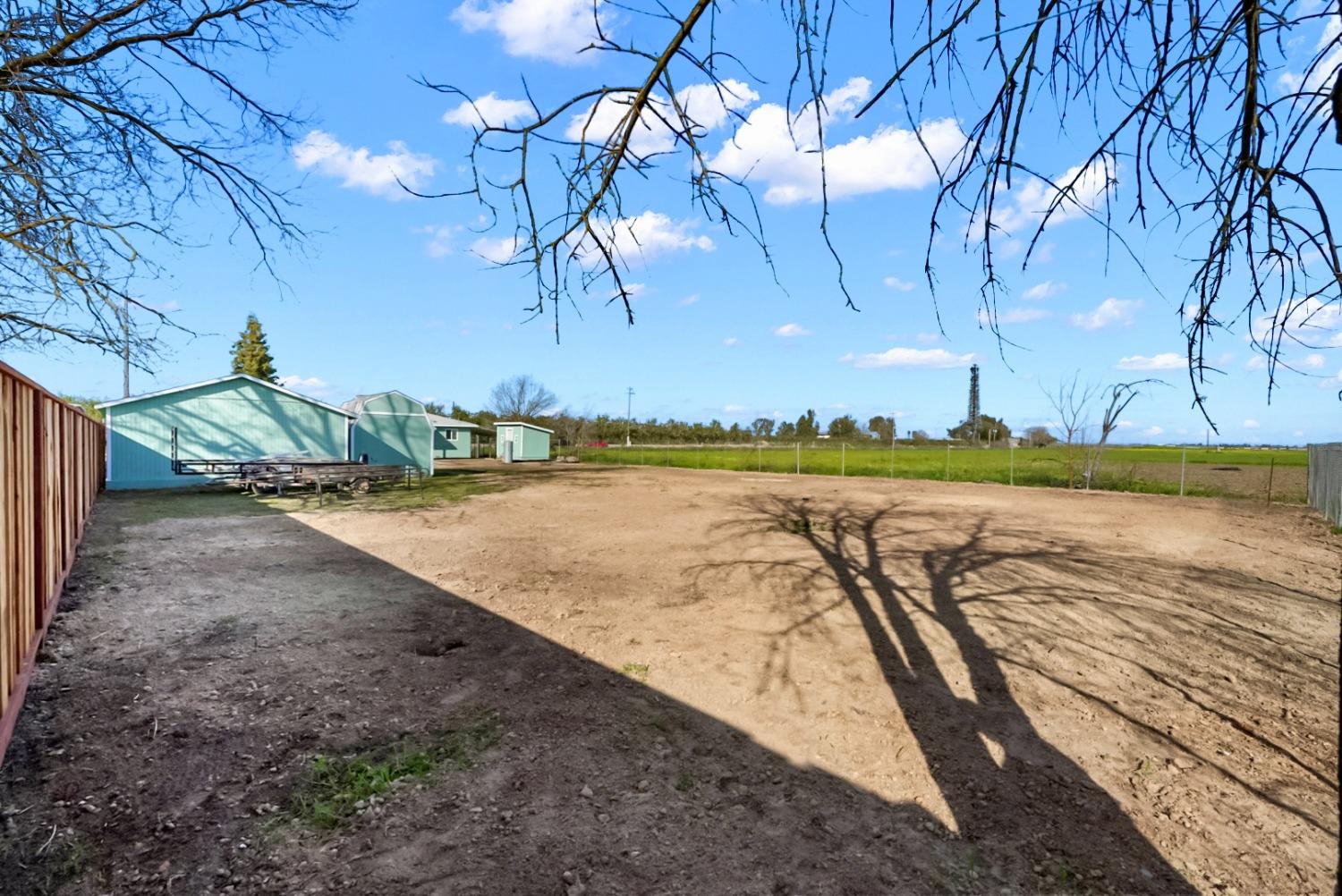 Dirt yard with light green outbuildings, fenced fields, and bare tree branches overhead.