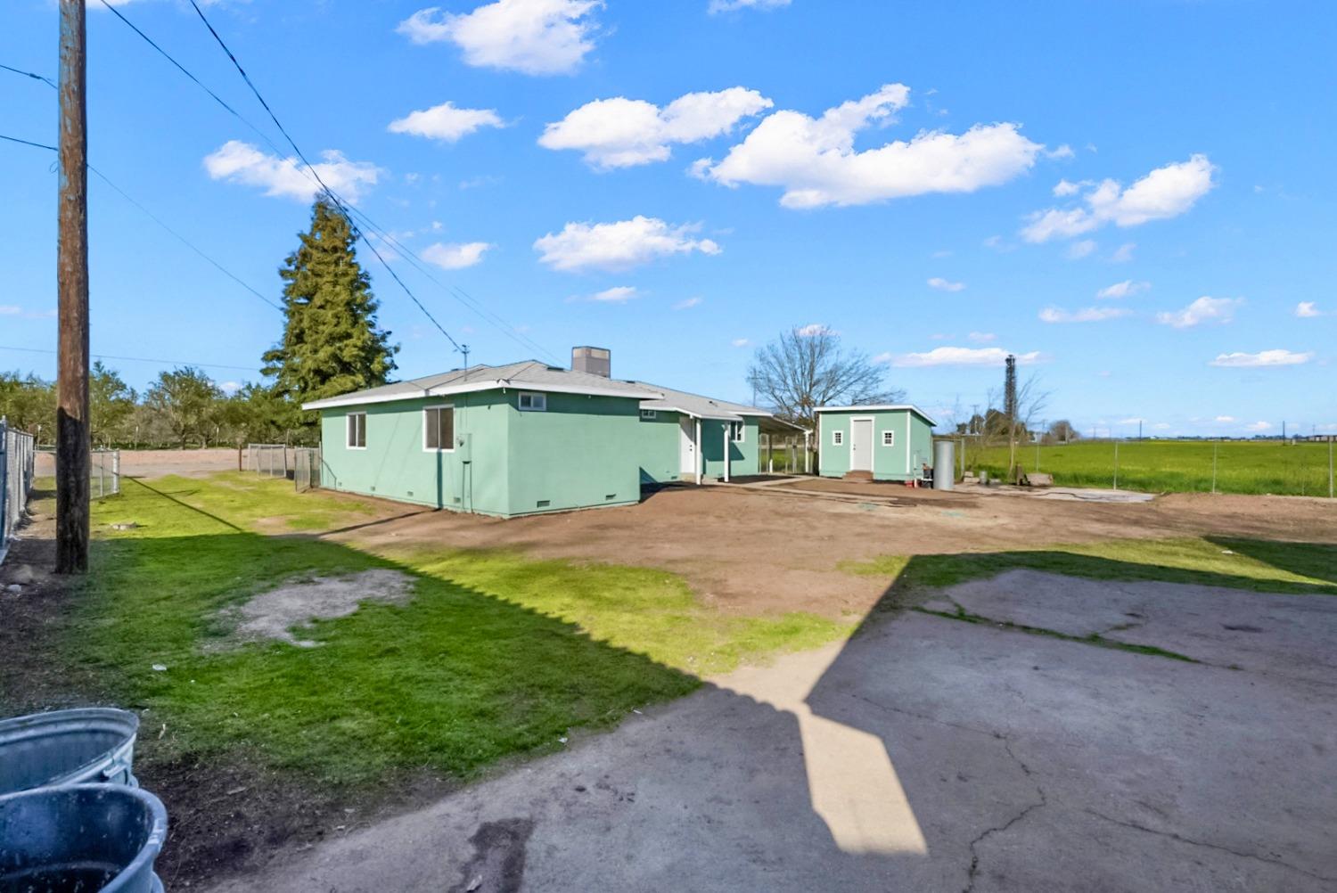Mint-green single-story home and detached outbuilding beside open farmland.