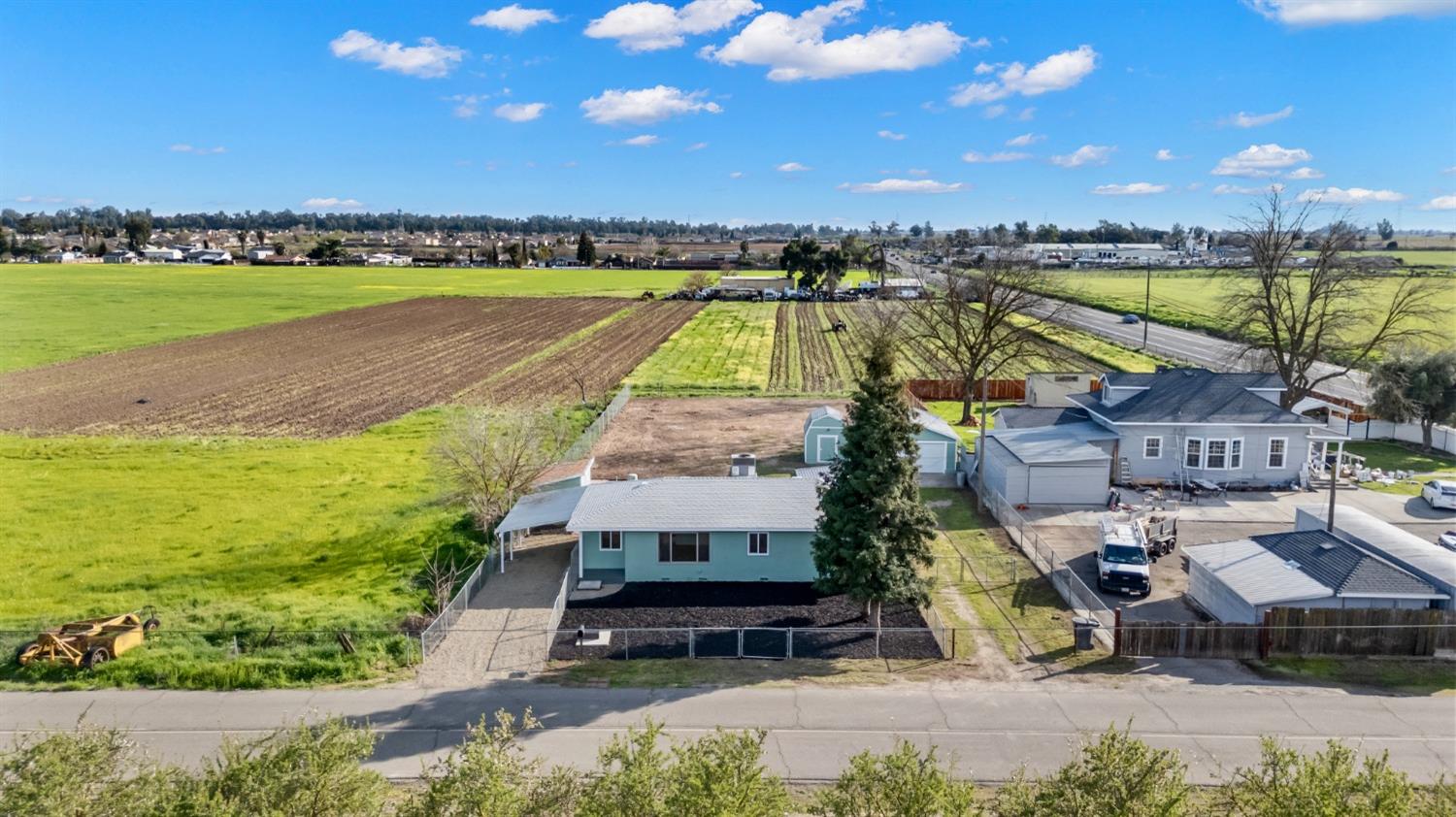 Aerial view of a single-story home beside cultivated fields, with a fenced yard and driveway.
