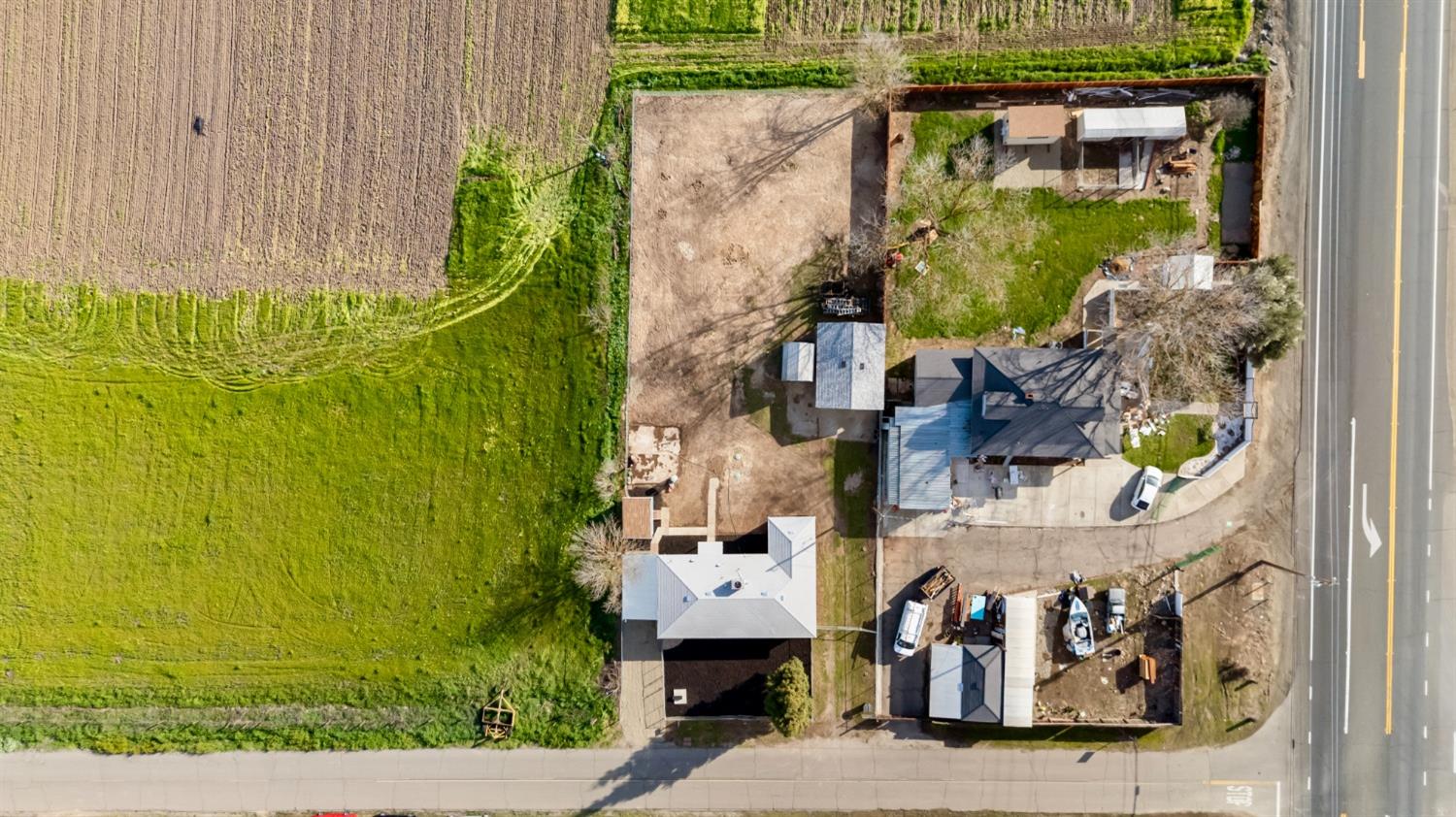 Aerial view of a corner property with several buildings, paved areas, and a large green field beside it.