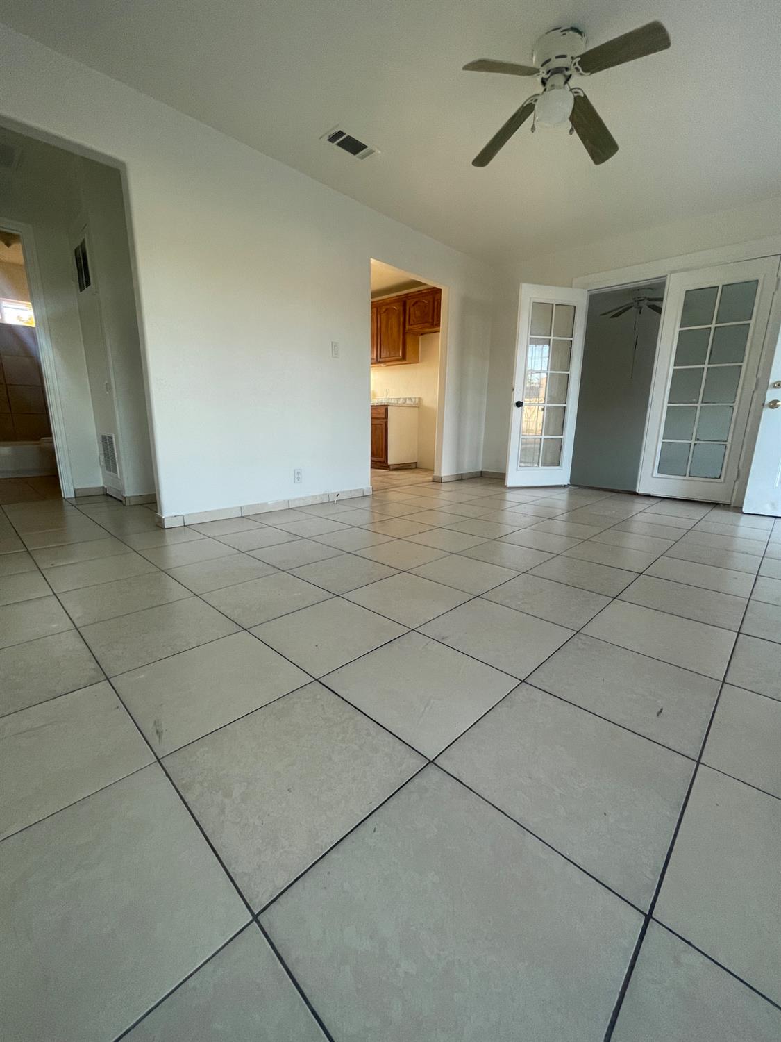 Empty living room with tiled floors, a ceiling fan, and French doors.