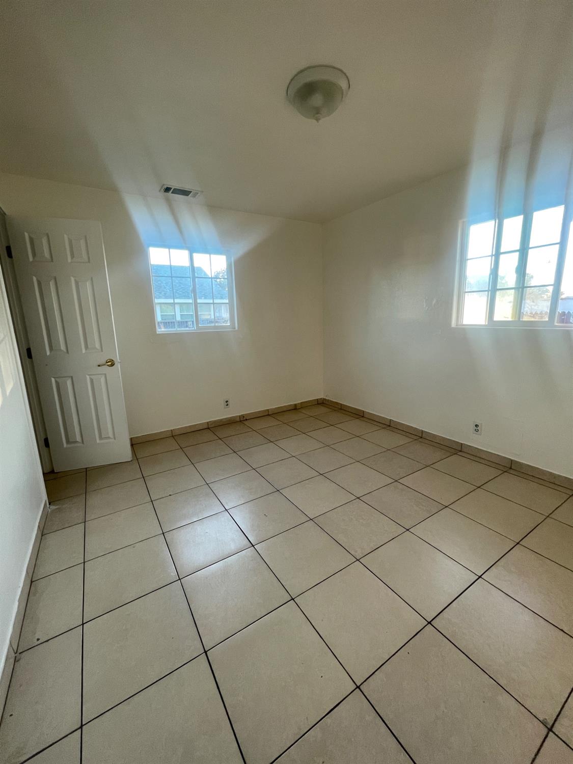 Empty room with beige tile flooring and two windows.