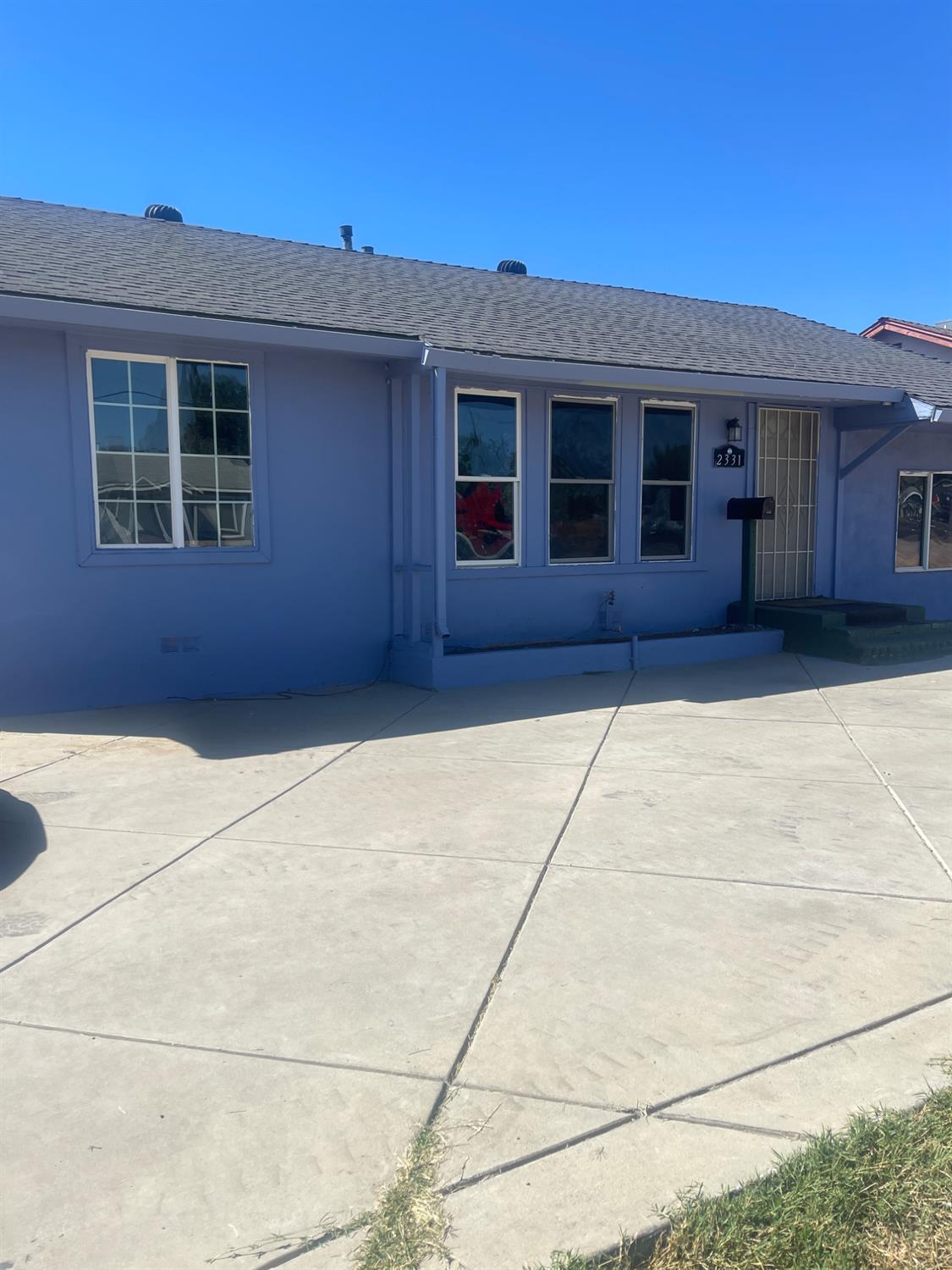 Blue single-story house with white-trimmed windows, security screen door, and broad concrete driveway.