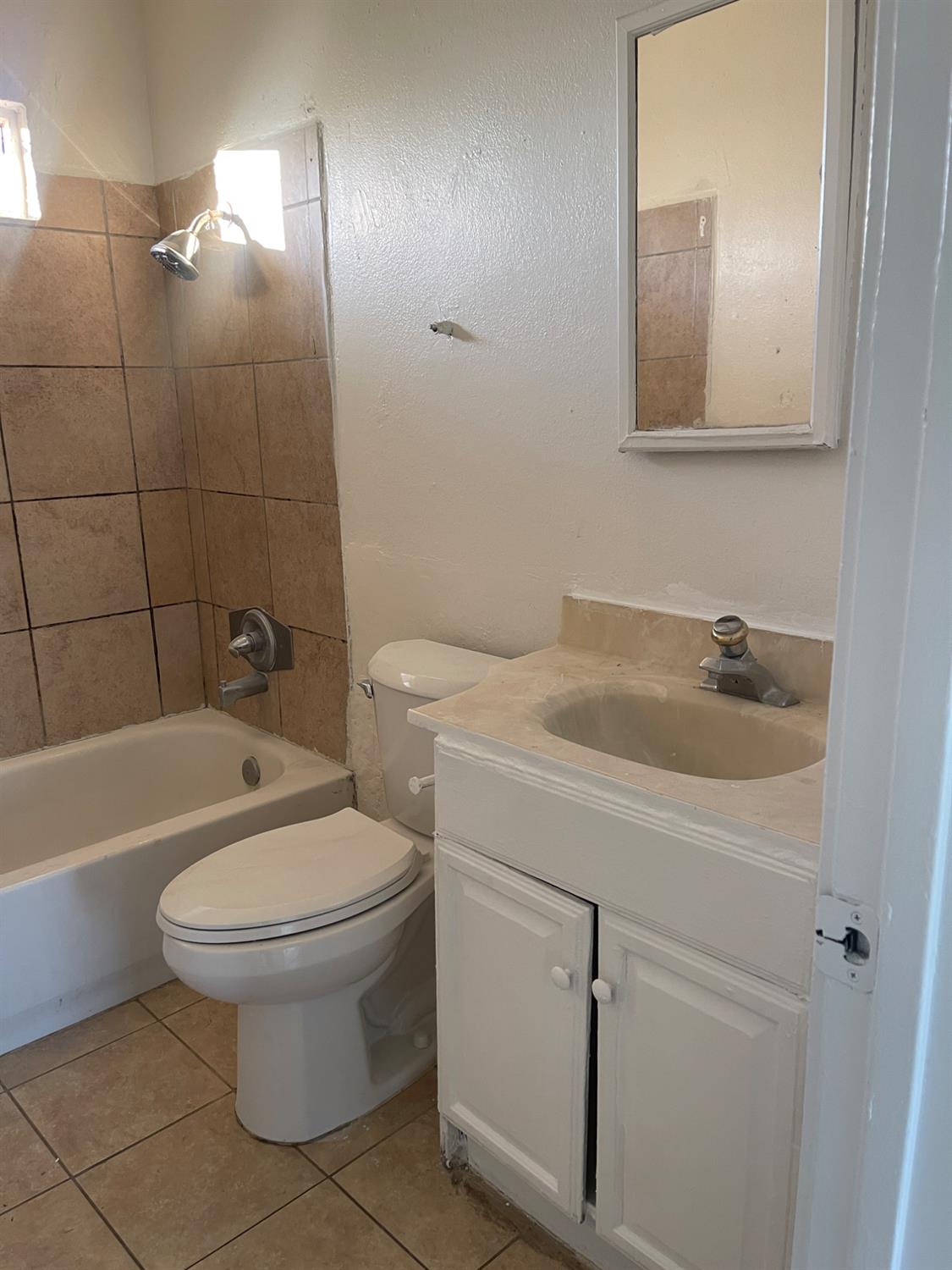 Bathroom with a tiled tub and shower, toilet, white vanity, and wall mirror.