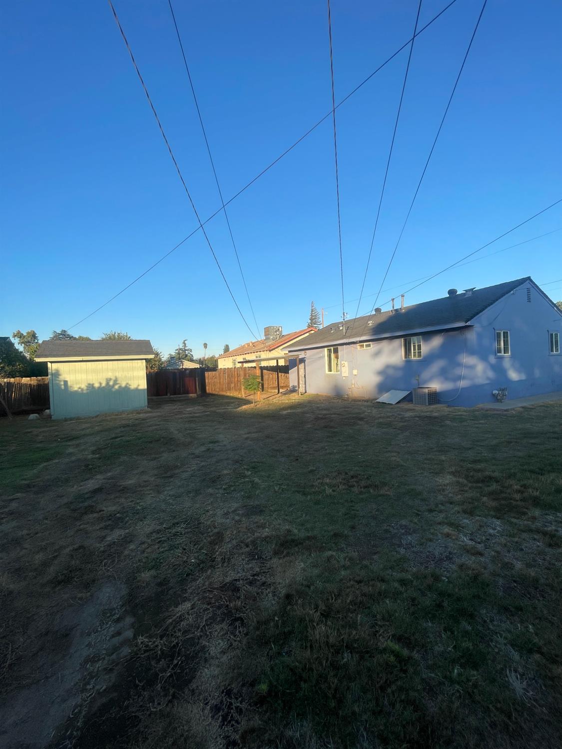 Blue single-story house and detached shed beside a mostly bare backyard.