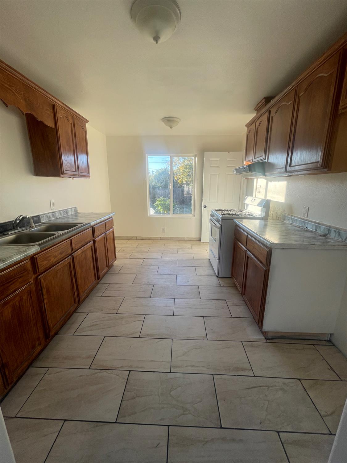 Vacant kitchen with dark wood cabinets, a double sink, gas range, and large tiled floor.