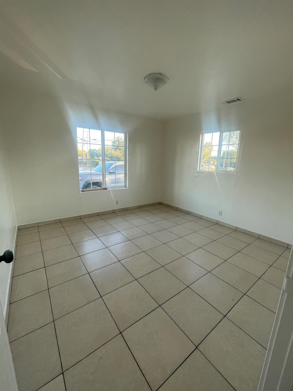Empty tiled room with two windows and sunlight streaming across the floor.