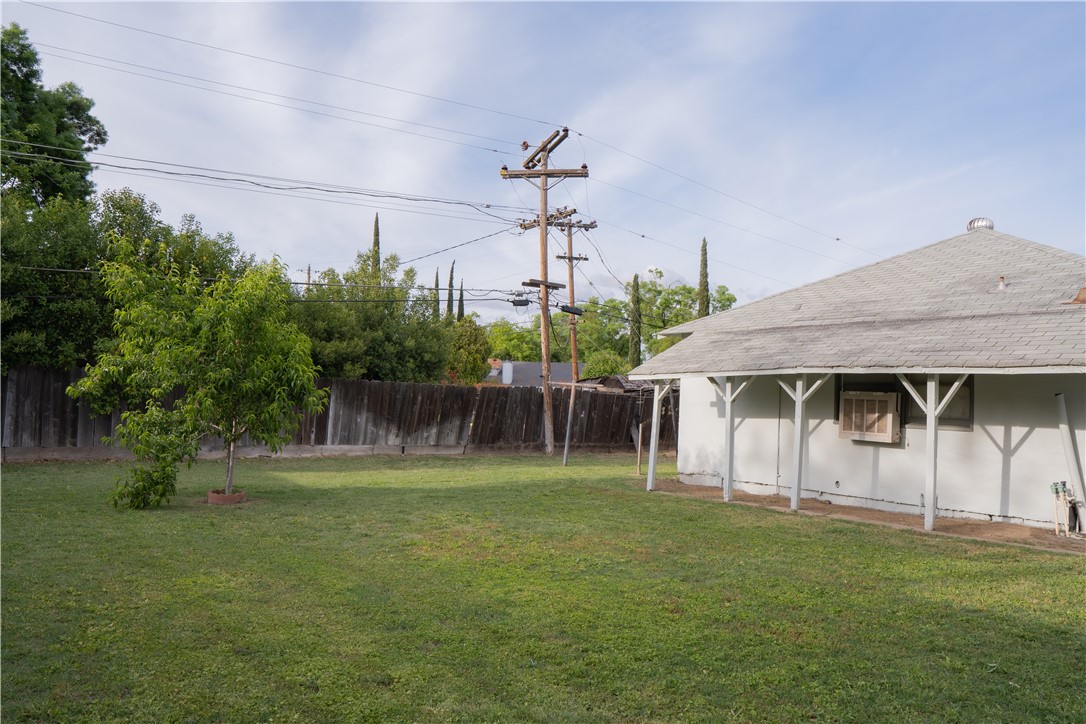 Backyard with a grassy lawn, small tree, wooden fence, and white house with roof supports.