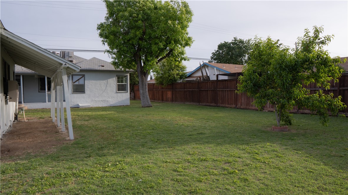 Backyard with a broad lawn, mature trees, wooden privacy fence, and covered patio.